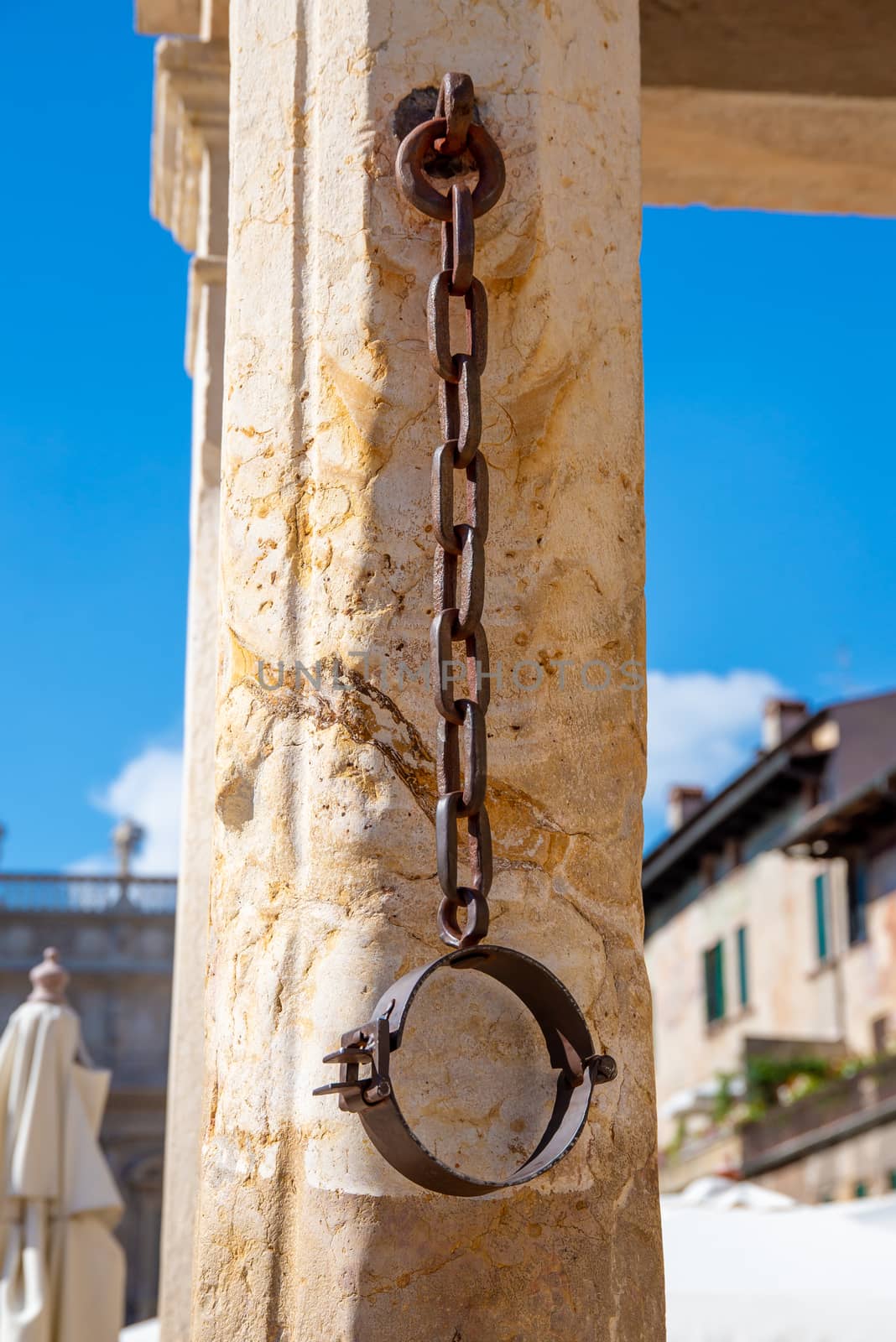 A metal neck iron on a pillory made of stone, which hangs down from a chain and where in former times prisoners were chained, who were put on the pillory