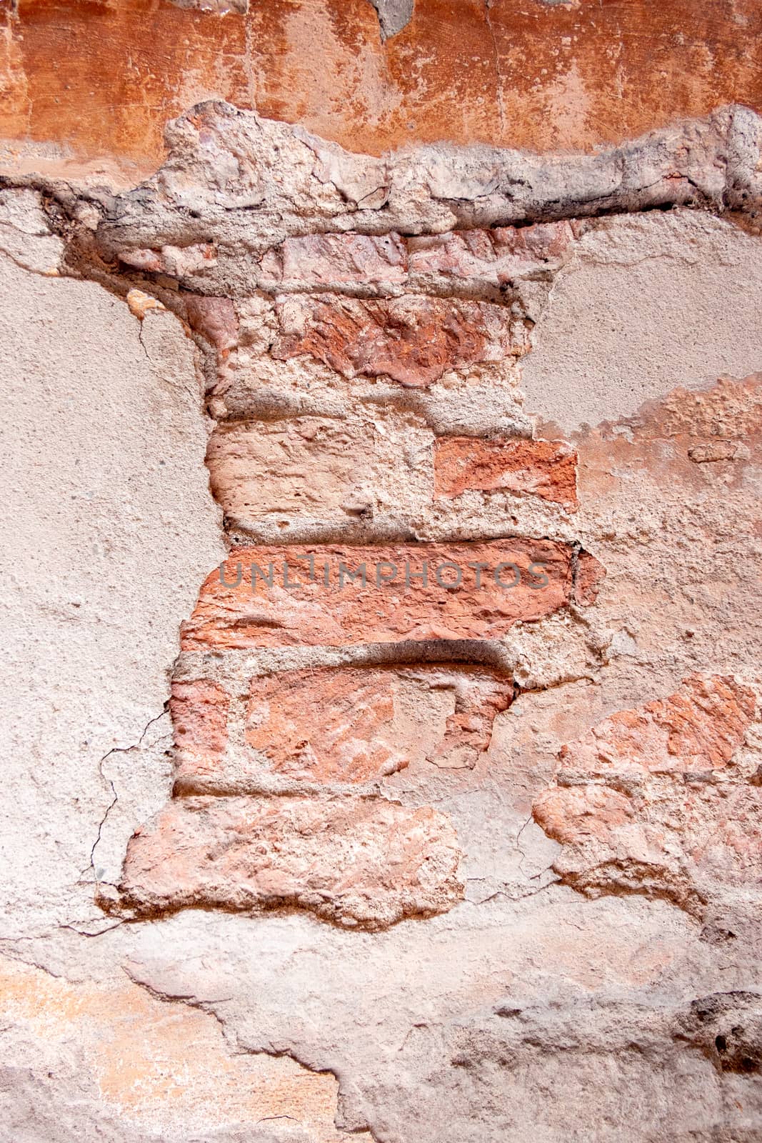 A wall of bricks with visible mortar between the bricks and many remnants of plaster that have already been flaked off.