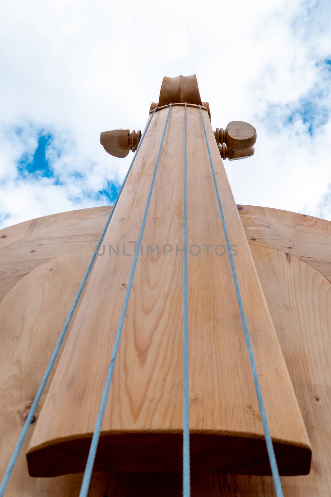 The fingerboard, sides and pegs of a huge violin or violin made of wood photographed from below against the sky.
