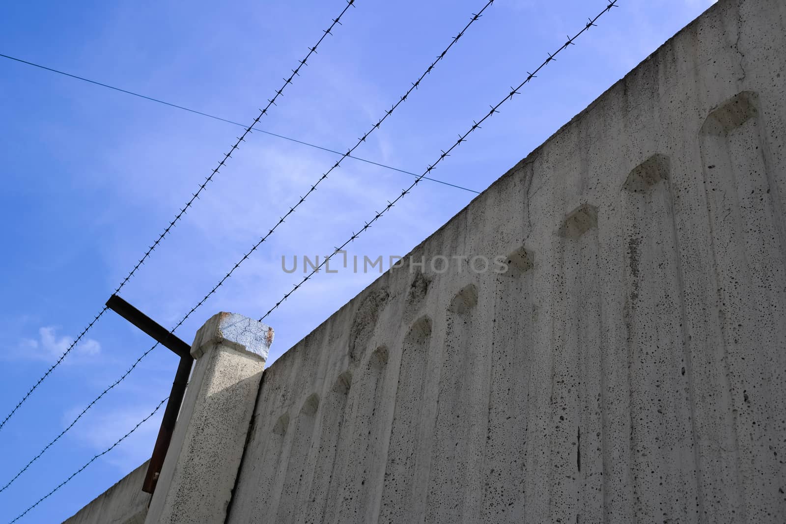 concrete fence with barbed wire against the blue sky