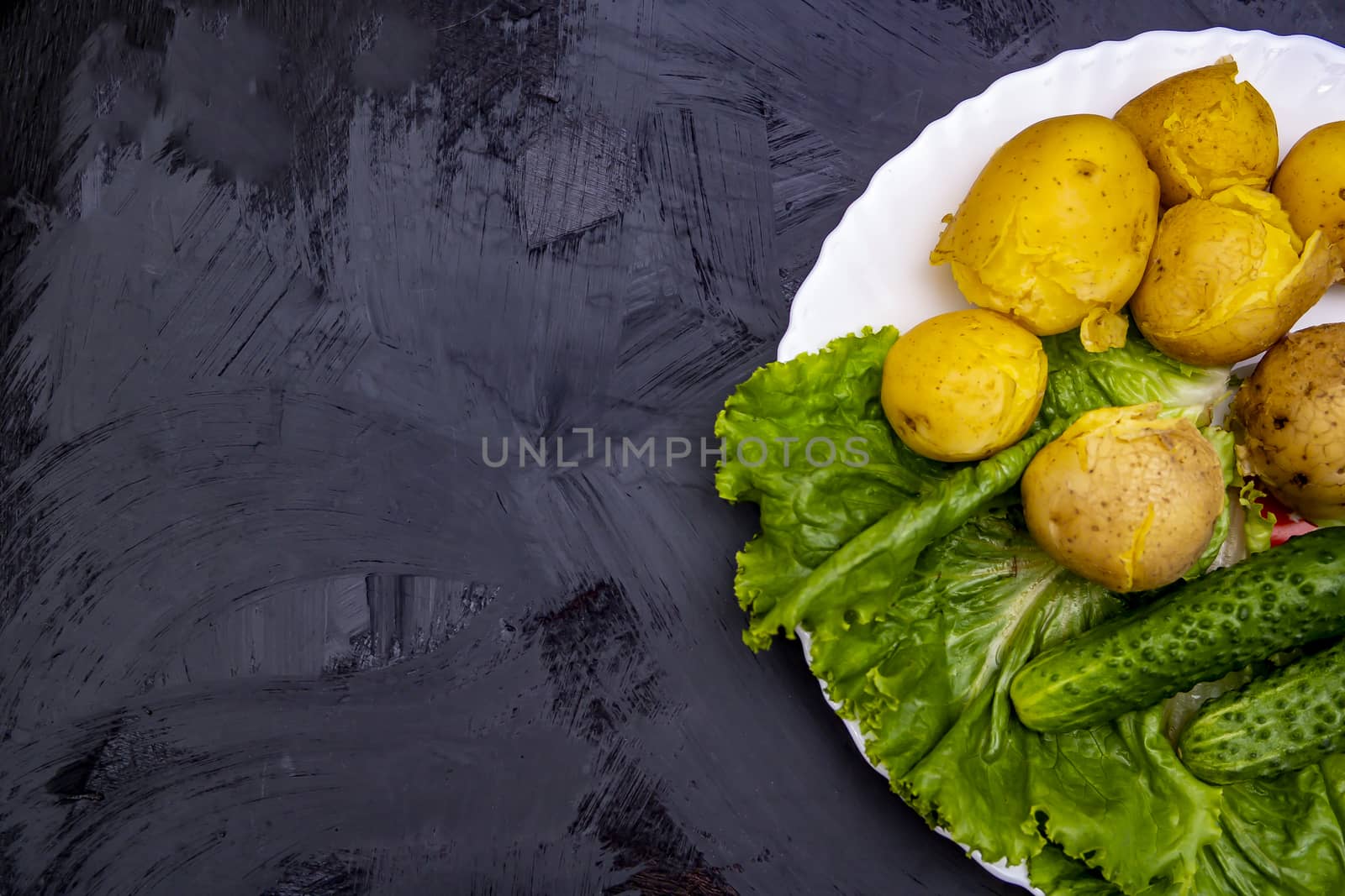 boiled potatoes with cucumber, lying on a white plate with lettuce with boiled potatoes