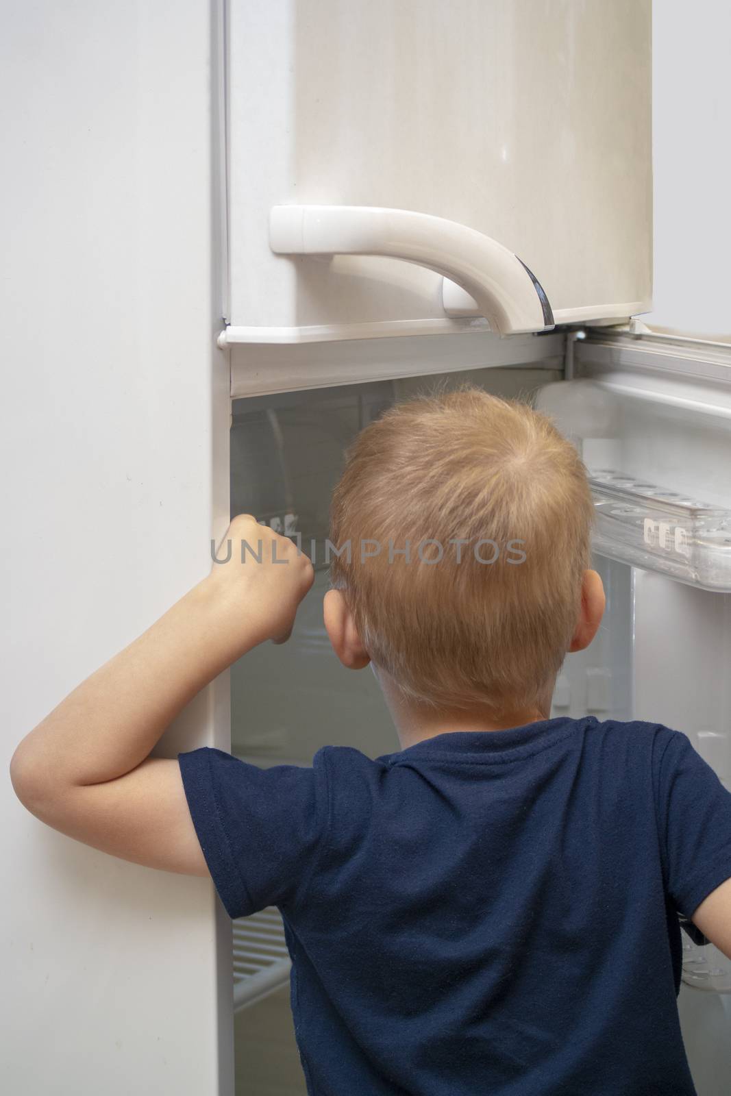 a small boy looks into an empty refrigerator for food.