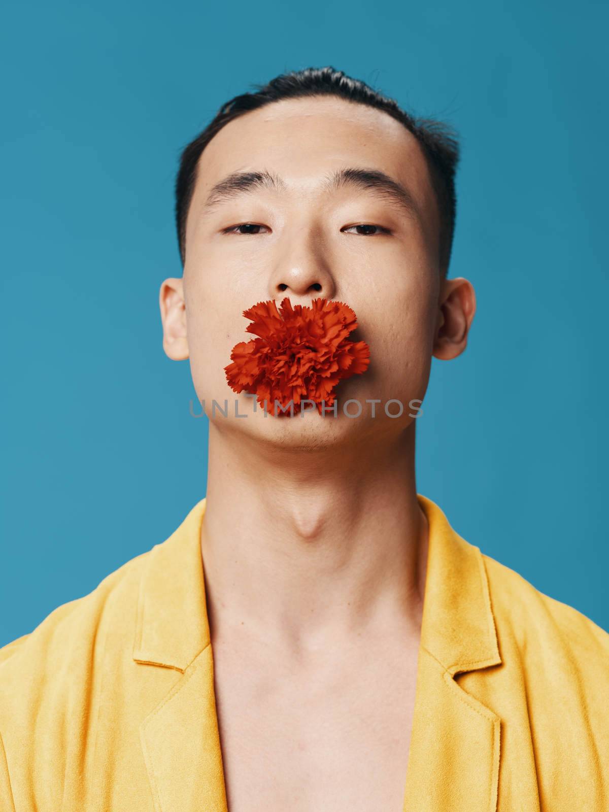 Asian man with red flower in teeth yellow coat bared torso close-up . High quality photo