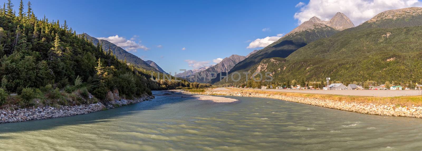 View of Skagway River and Skagway airport at sunset in Alaska. Golden hour. Blue cloudy sky and mountain peaks in the background.