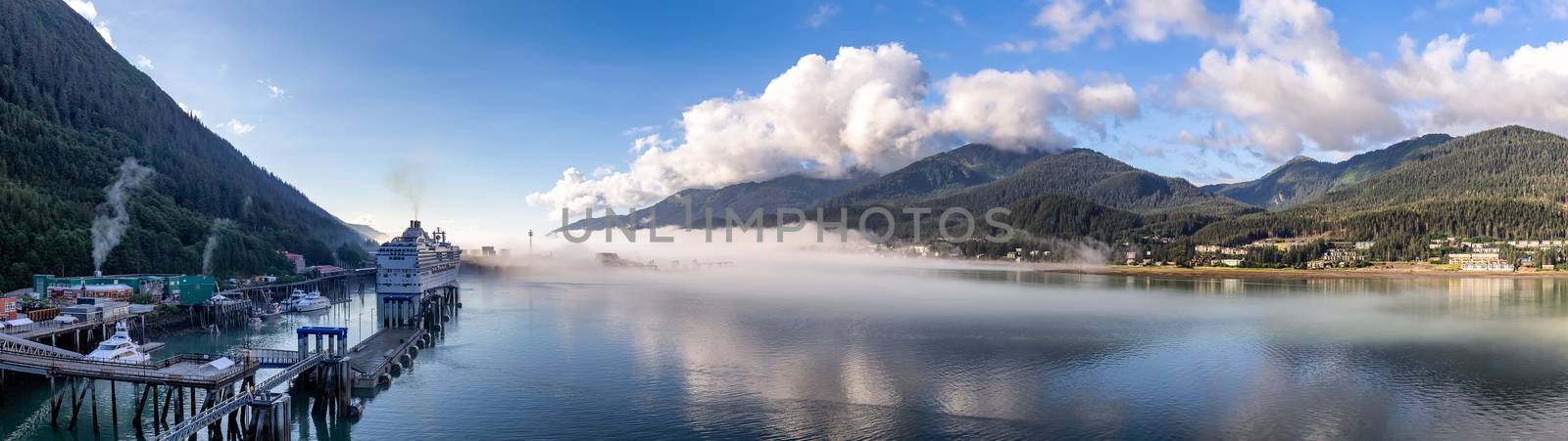 Panoramic shot of port of Juneau and mountains covered with clouds and fog in Gastineau Channel, Alaska. Cruise ship and boats docked in the port. Blue cloudy sky as a background.