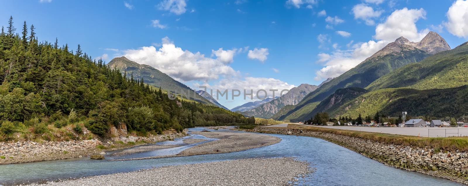 View of shallow Skagway River and Skagway airport in Alaska. Blue cloudy sky and mountain peaks in the background by DamantisZ