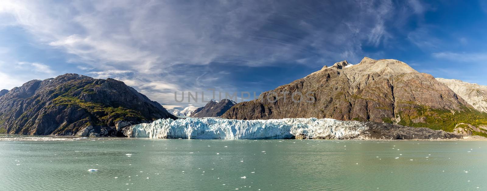 Panoramic view of Margerie glacier surrounded by huge mountains in Glacier Bay National Park and Preserve, Alaska, United States. Snowy mountain peaks and cloudy blue sky in the background by DamantisZ