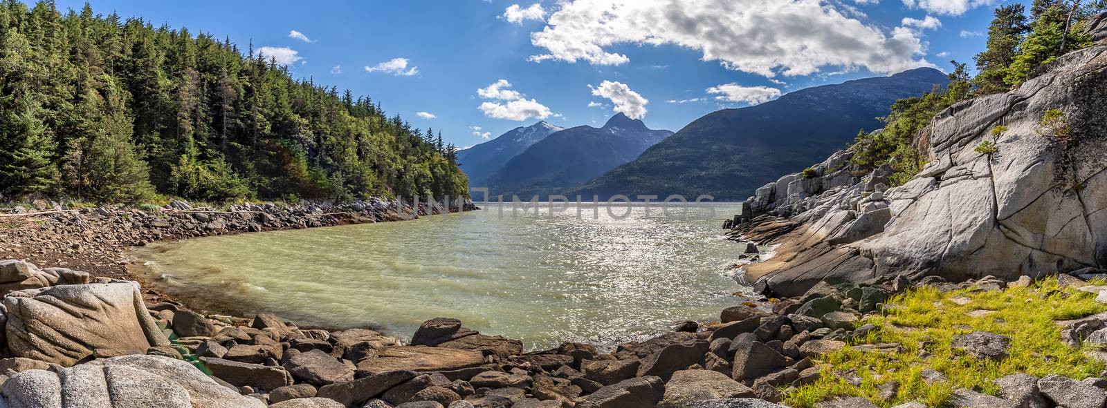 Beautiful panoramic view of Smuggler's Cove in Alaska. Mountains, forest, blue cloudy sky in the background. Rocky terrain in the foreground.