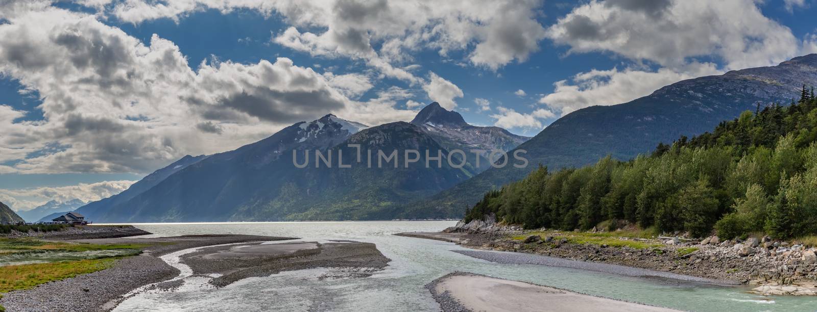 Panoramic shot of Yucatania point and shallow Skagway river in Skagway, Alaska. Mountains and cloudy blue sky as a background by DamantisZ