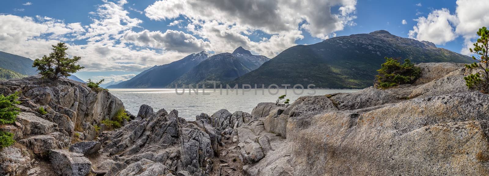 Panoramic shot from Yucatania point near Skagway, Alaska. Rocky terrain as a foreground. Mountains and cloudy blue sky as a background.