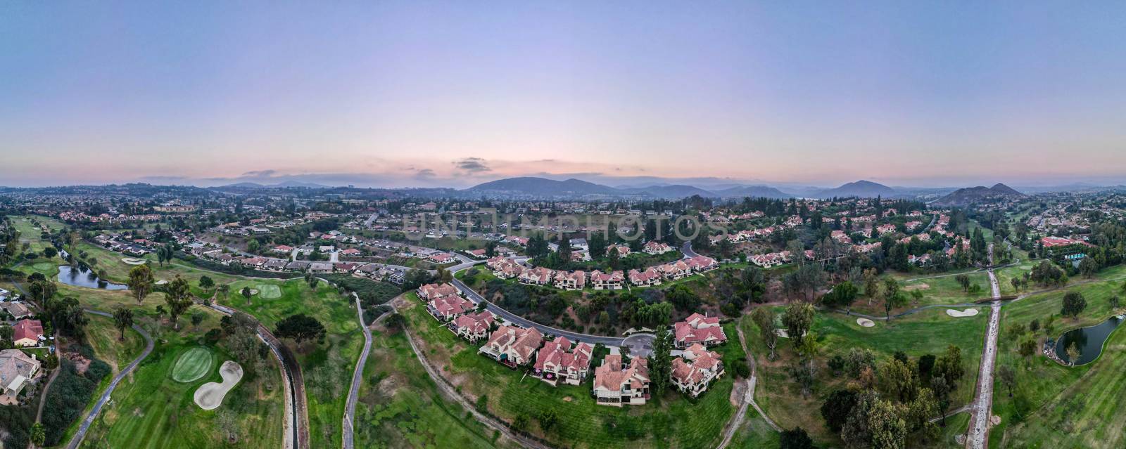Aerial panoramic view of golf in upscale residential neighborhood during sunset by Bonandbon