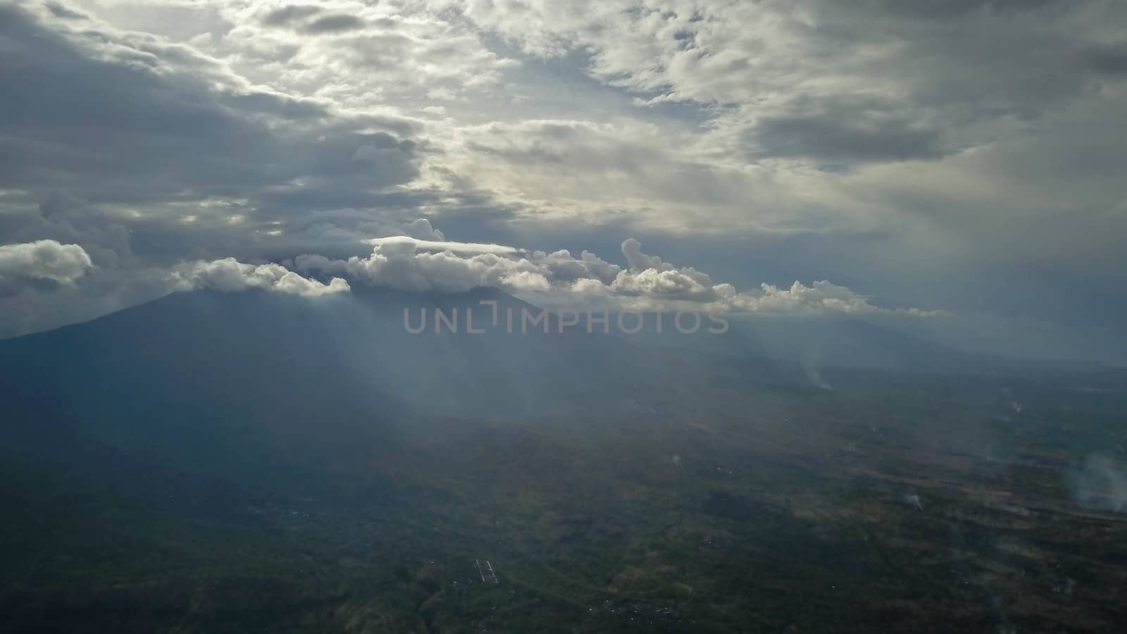volcano with cloudy clear sky. Mount Merapi in Indonesia. Cloudy sky with a volcano in the background. Clouds around the top of the mountain. The sun's rays shine through the clouds.