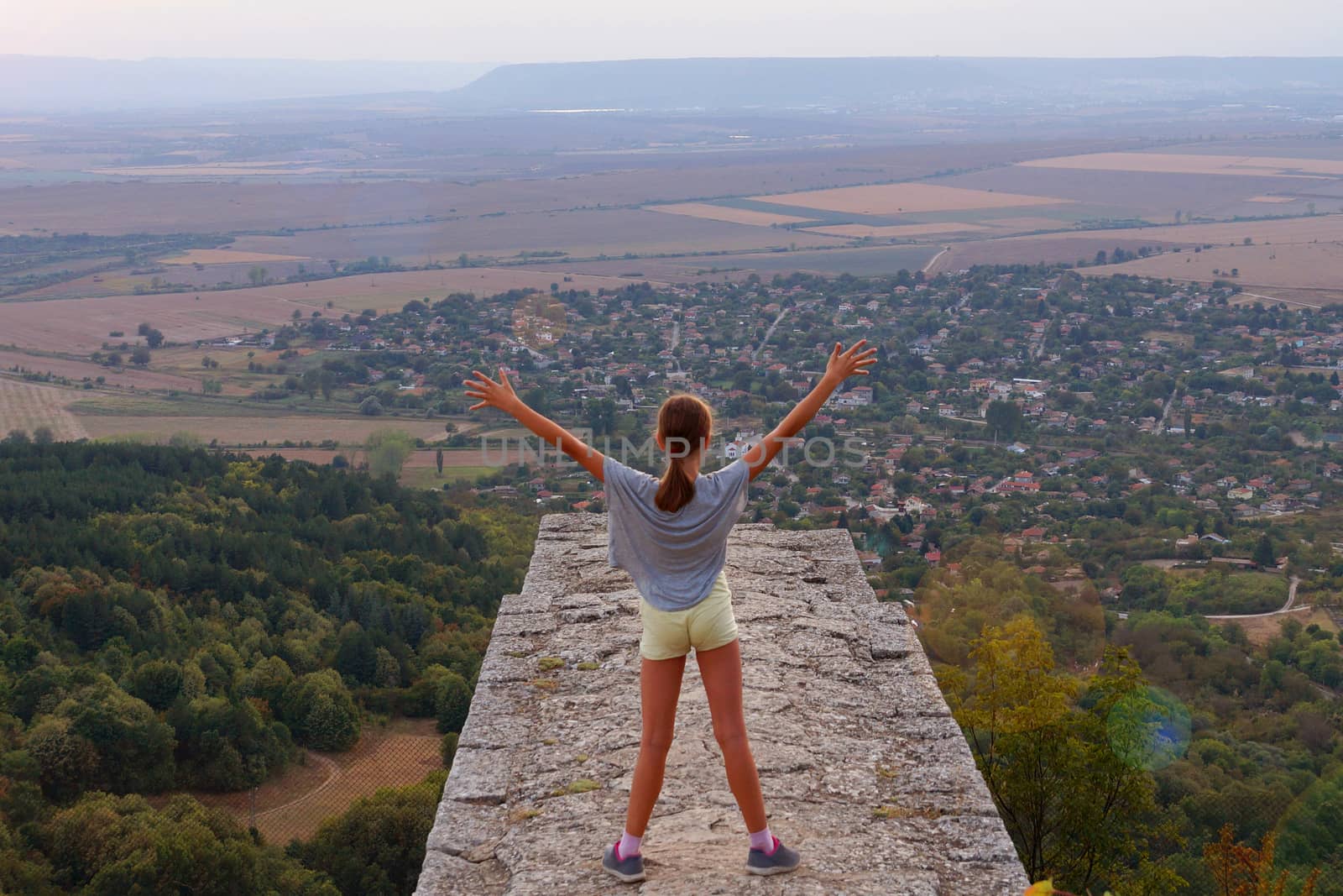 Girl standing at height, arms outstretched to the sky, rear view