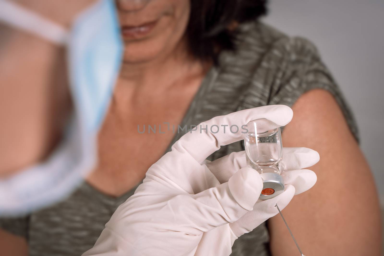 Nurse wearing gloves holding a vaccine vial. In the background a patient waiting for the vacuum