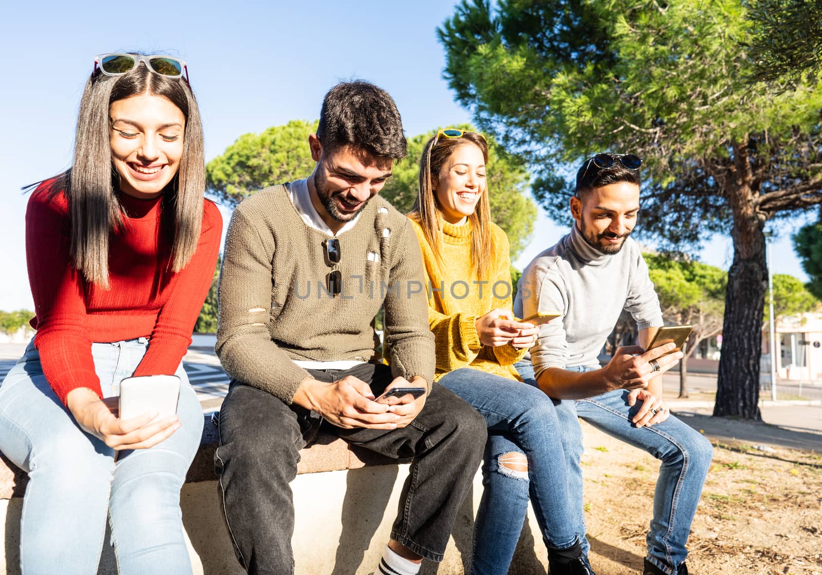 Two beautiful young couple sitting on a wall having fun using smartphone - Friends group smiling looking at the cell phone for chatting in social network - New generations technology social contacts by robbyfontanesi