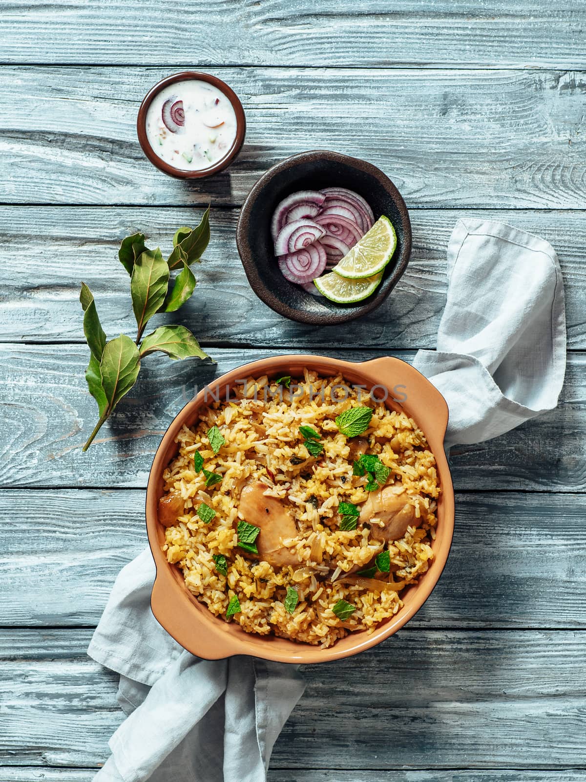 Pakistani food - biryani rice with chicken and raita yoghurt dip. Delicious hyberabadi chicken biryani on gray wooden background. Top view or flat lay. Copy space. Vertical.