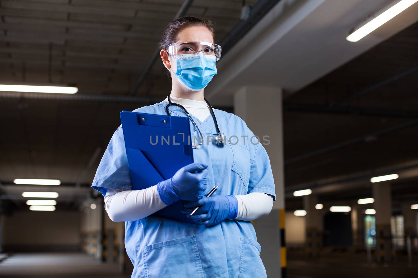 Medical EMS worker wearing PPE uniform,safety goggles and face mask,holding clipboard at mobile test center site,PCR Coronavirus COVID-19 virus disease detection in drive-thru check & control facility