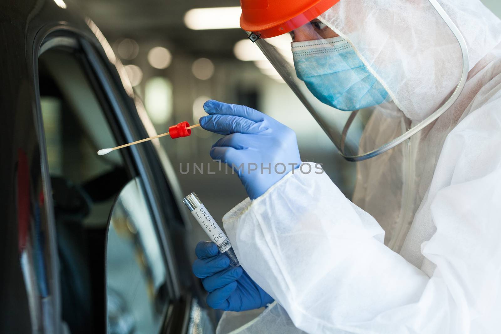 Medical NHS worker in personal protective equipment swabbing a person in a car drive through Coronavirus COVID-19 mobile testing center,oral and nasal specimen collection procedure,health and safety 