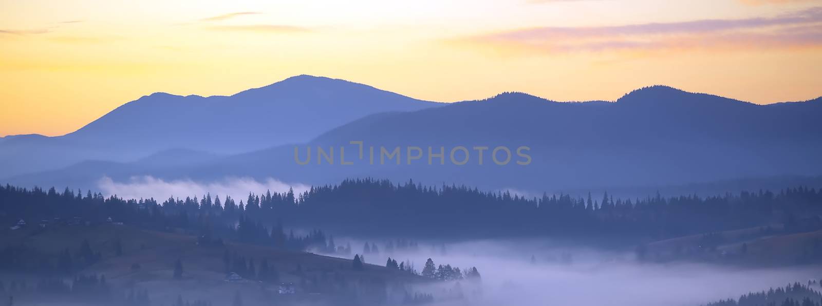 Panorama morning fog in the mountains. Dawn in the mountains. The morning sun in the fog. Colorful dawn panoramic.