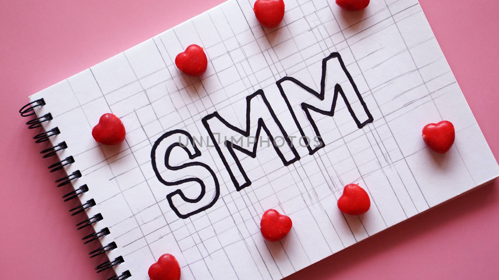 SMM Social media marketing text on on notebook on pink background with candy in the form of hearts