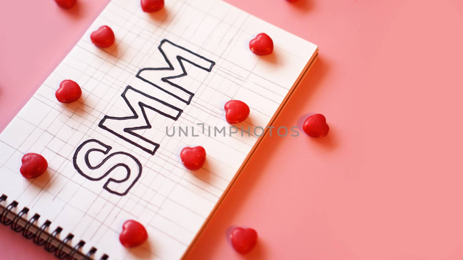 SMM Social media marketing text on on notebook on pink background with candy in the form of hearts