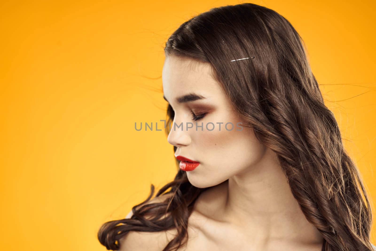 Beautiful brunette naked shoulders bright makeup red lips hairstyle close-up yellow background. High quality photo