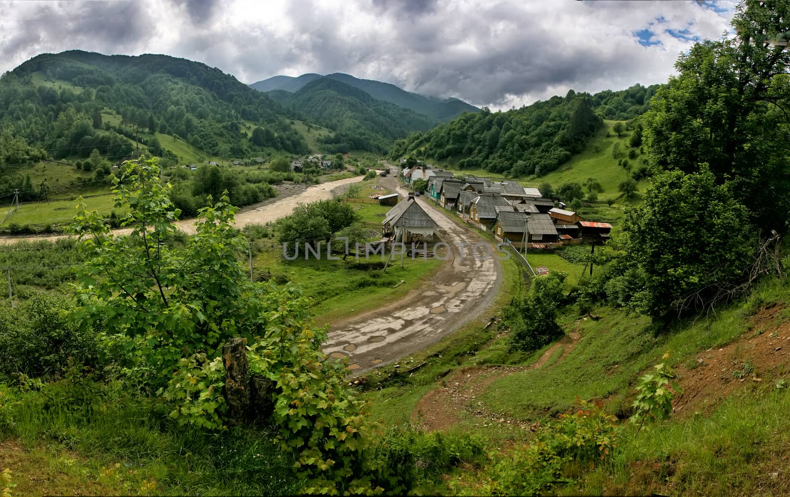 Ecotourism. Rural landscape. An old village in a picturesque place among the hills and mountains overgrown with green trees. The road passes through the village.