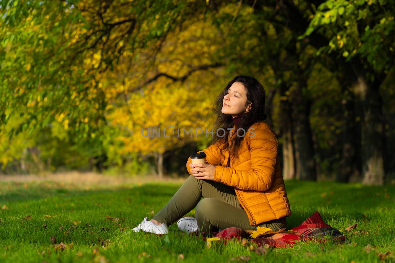 Pretty girl enjoys autumn and the beauty of nature sitting on a green lawn in the park. Autumn mood.