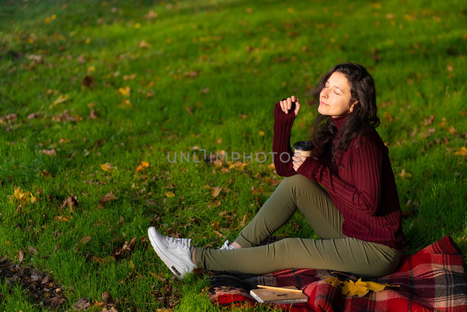 Pretty girl enjoys autumn and the beauty of nature sitting on a green lawn in the park. Autumn mood.