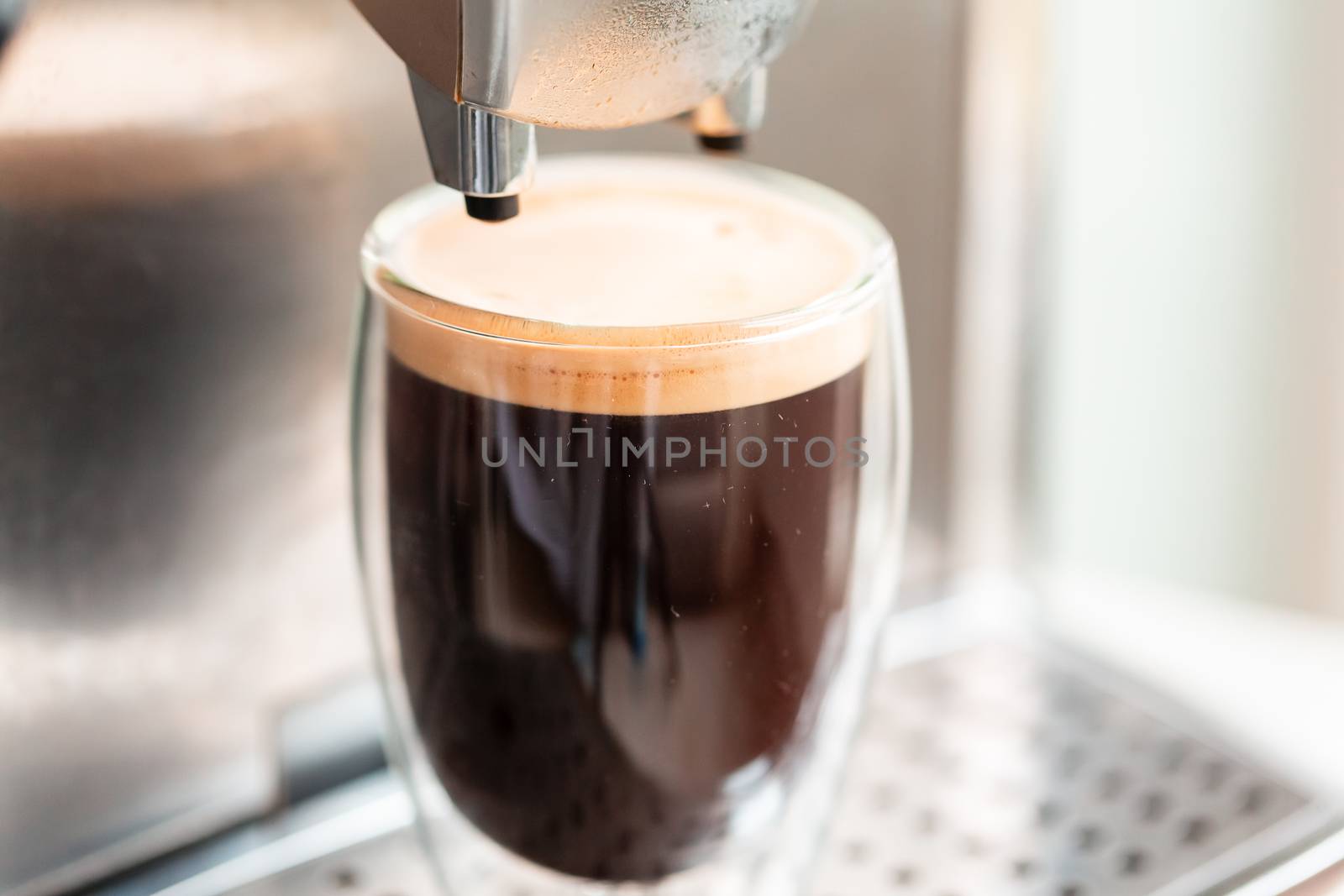 Coffee espresso streaming from coffee machine and pouring into glass. Home making hot Espresso. Flowing fresh ground coffee. Drinking roasted black coffee in the morning.