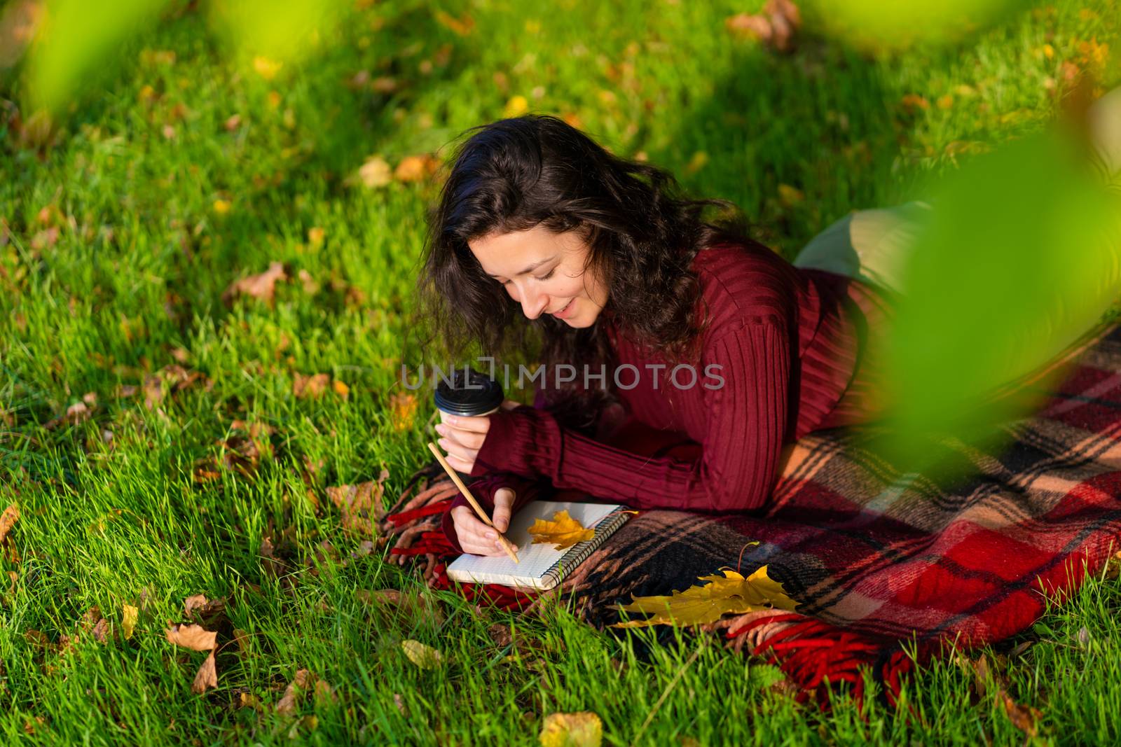 Person writes notes lying on the lawn in the autumn park. Solitude with yourself.