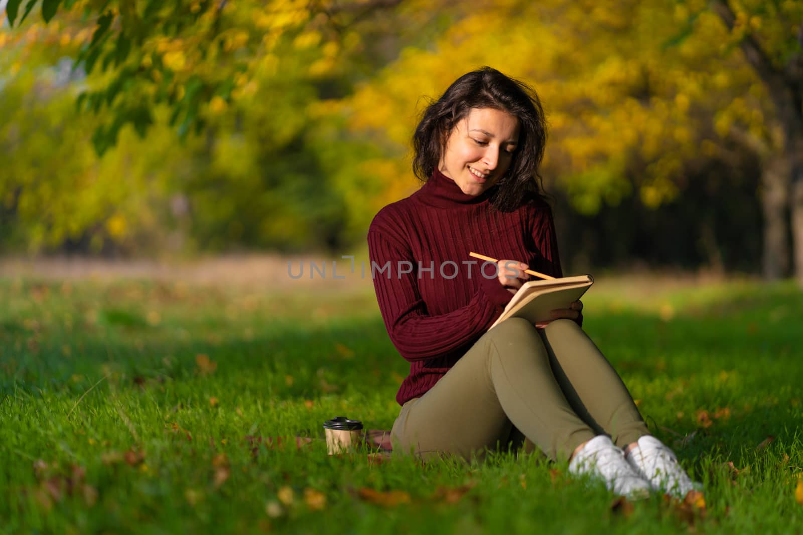 A person write notes sitting on a lawn in an autumn park. Joyful state of mind. Looking for inspiration.