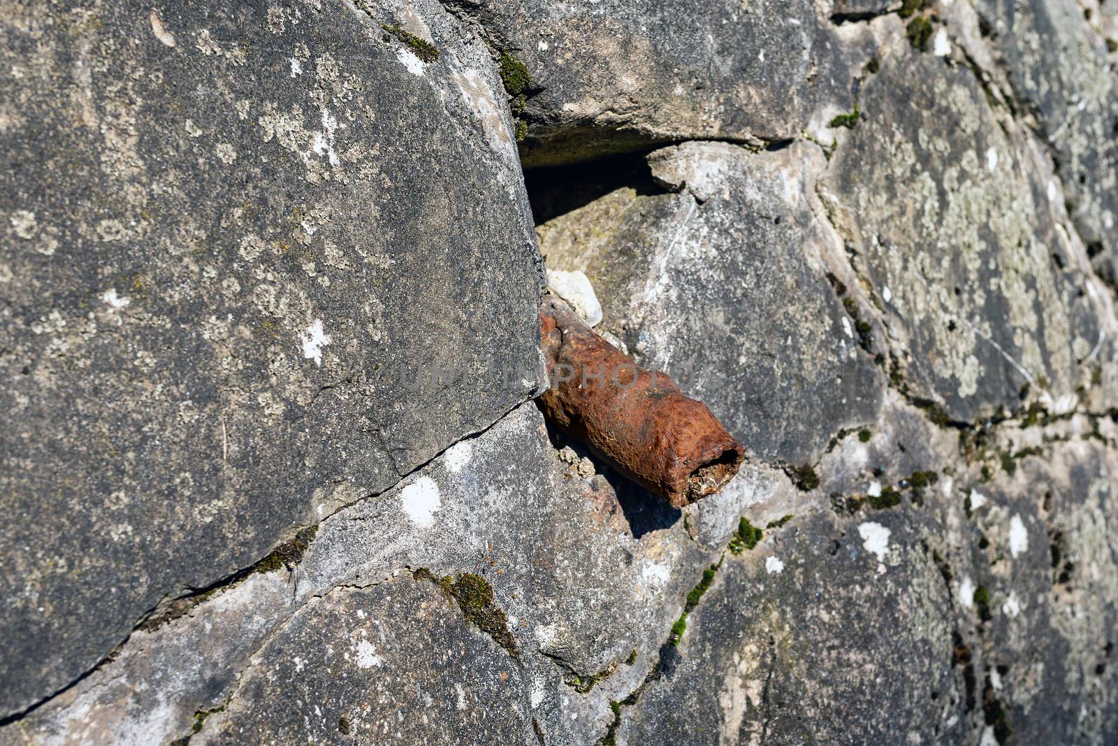 An old rusty pipe sticks out of a stone wall. Impotence, genital diseases in men concept. The tube looks like an old sore penis.