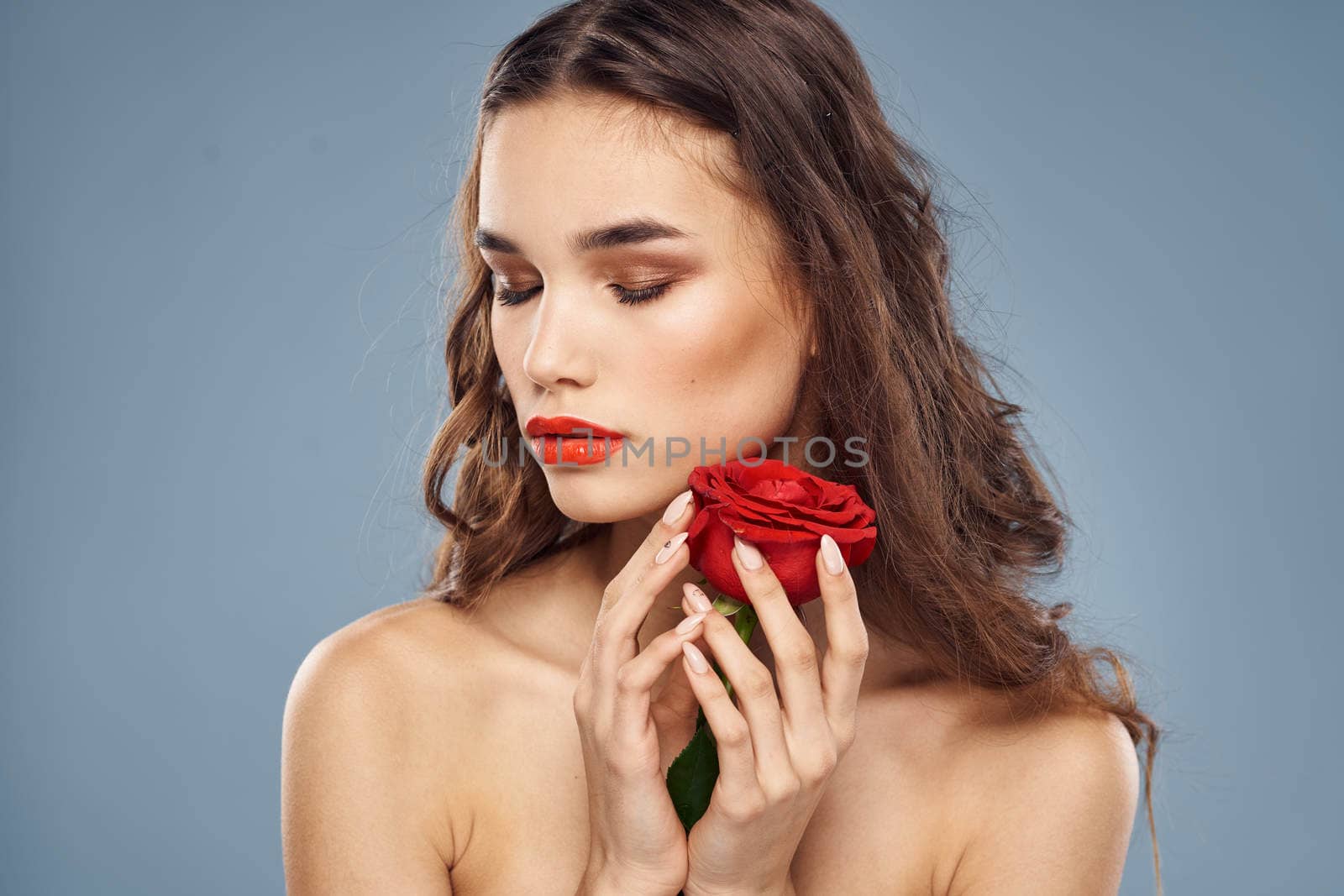 Woman portrait with red rose near the face on gray background and makeup curly hair. High quality photo