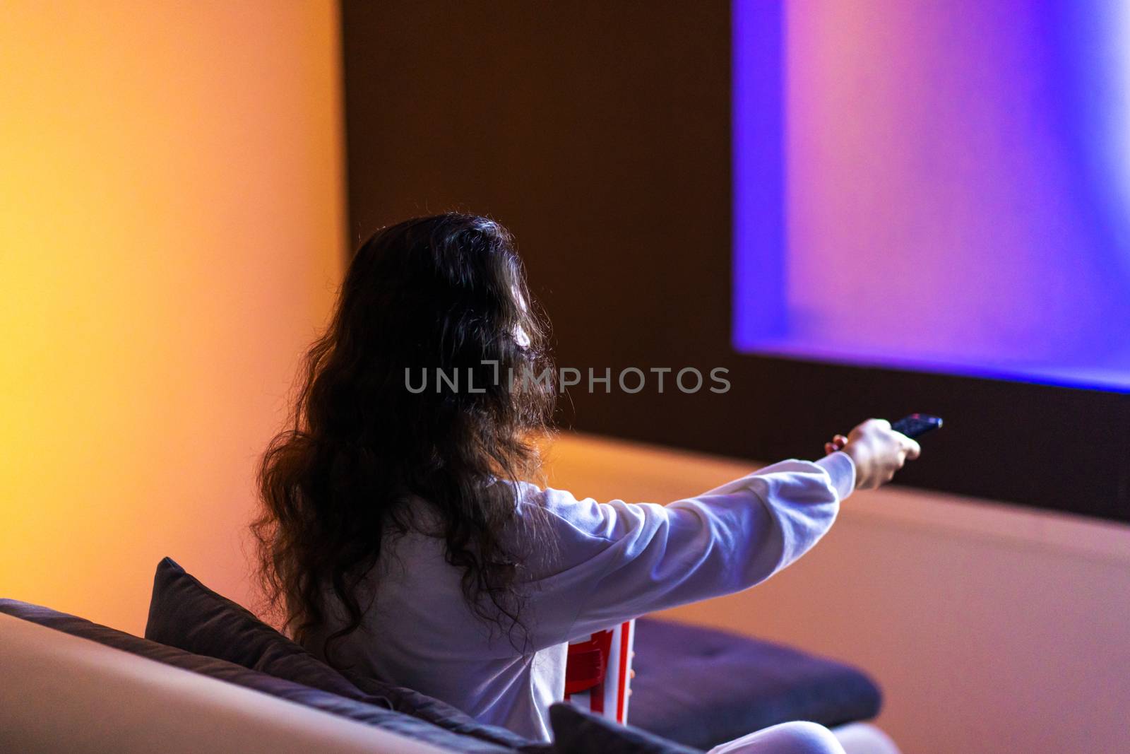 person watches a movie sitting on the couch with a bucket of popcorn.