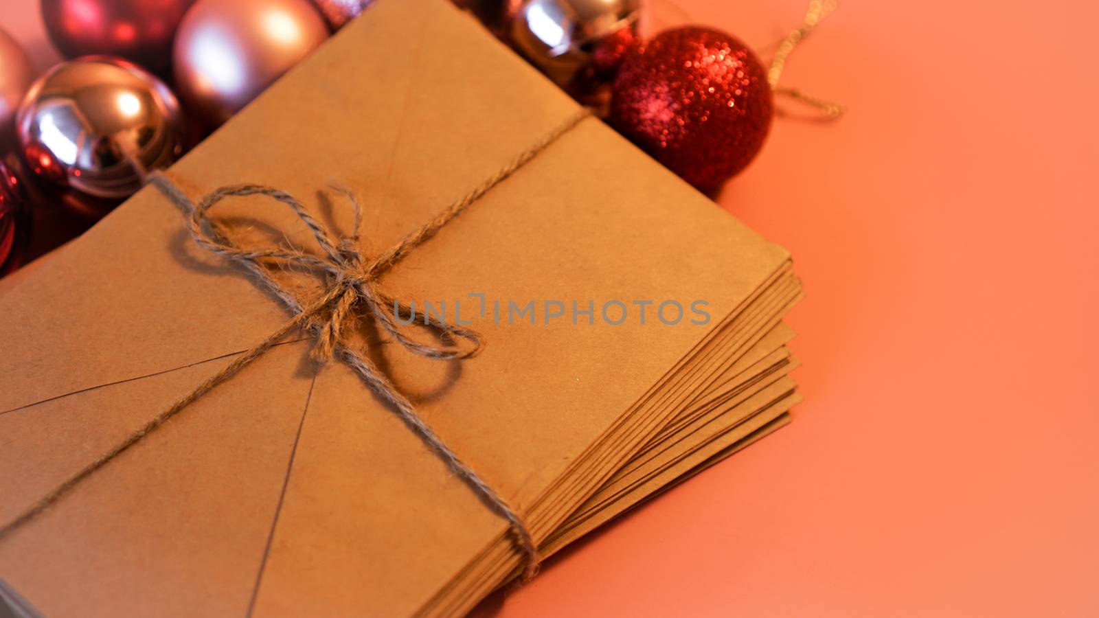 Stack of letters from craft paper with christmas red and pink balls on pink background