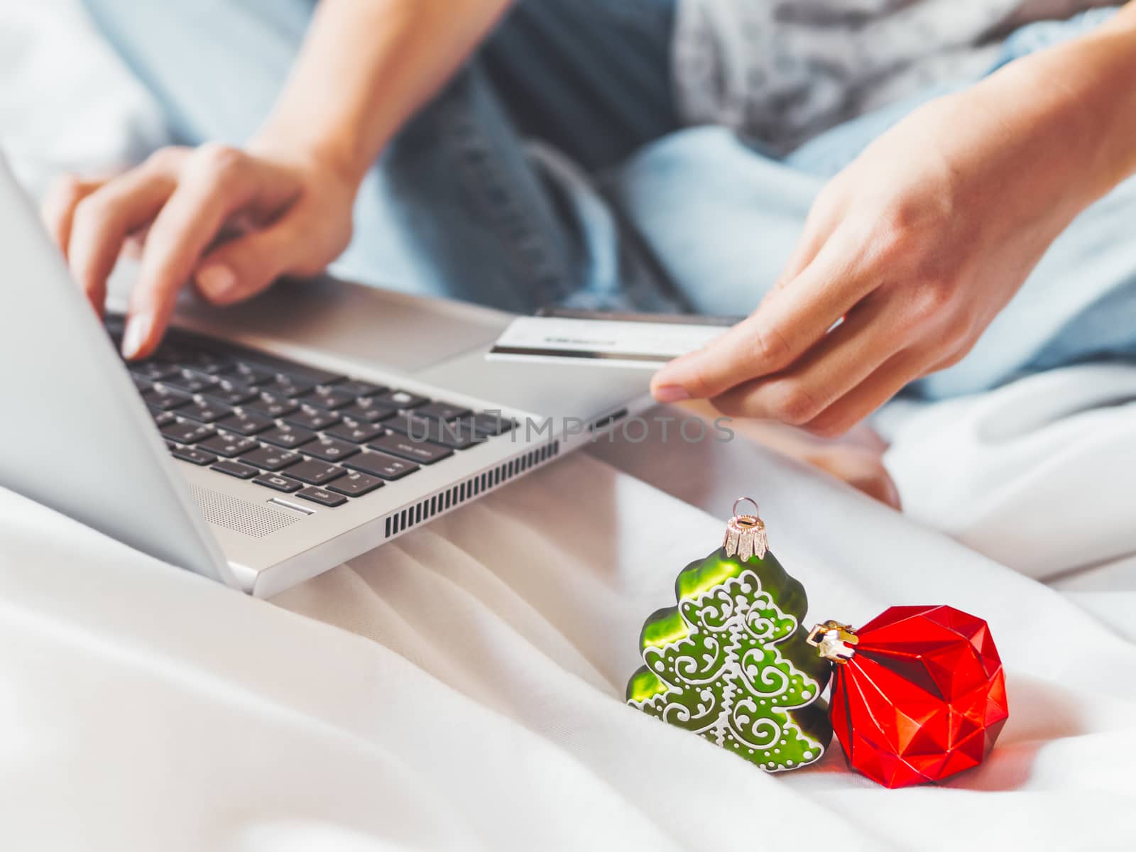 Woman using laptop to pay for online order by credit card. Decorative Christmas tree and New Year red ball in her hand. Online shopping before winter holidays.