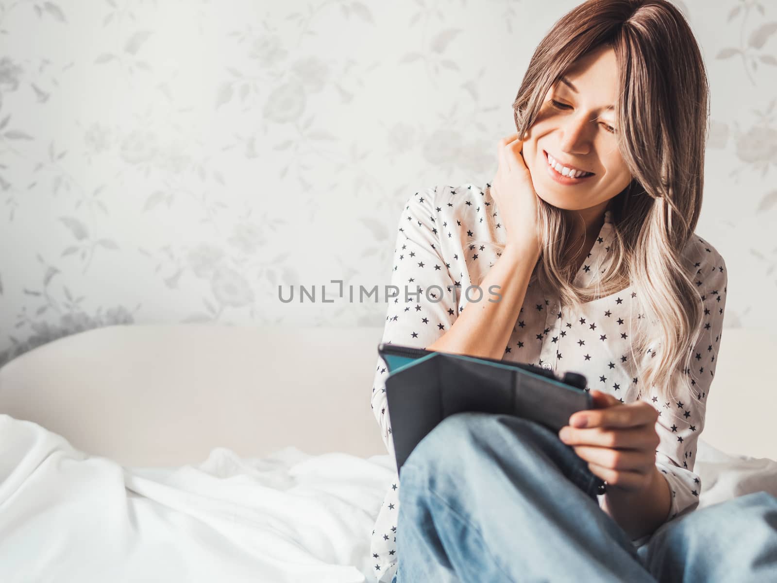 Woman sits on bed with tablet PC. She watches online TV series. Online video call or conference, distance learning, remote education. Self isolation during quarantine.