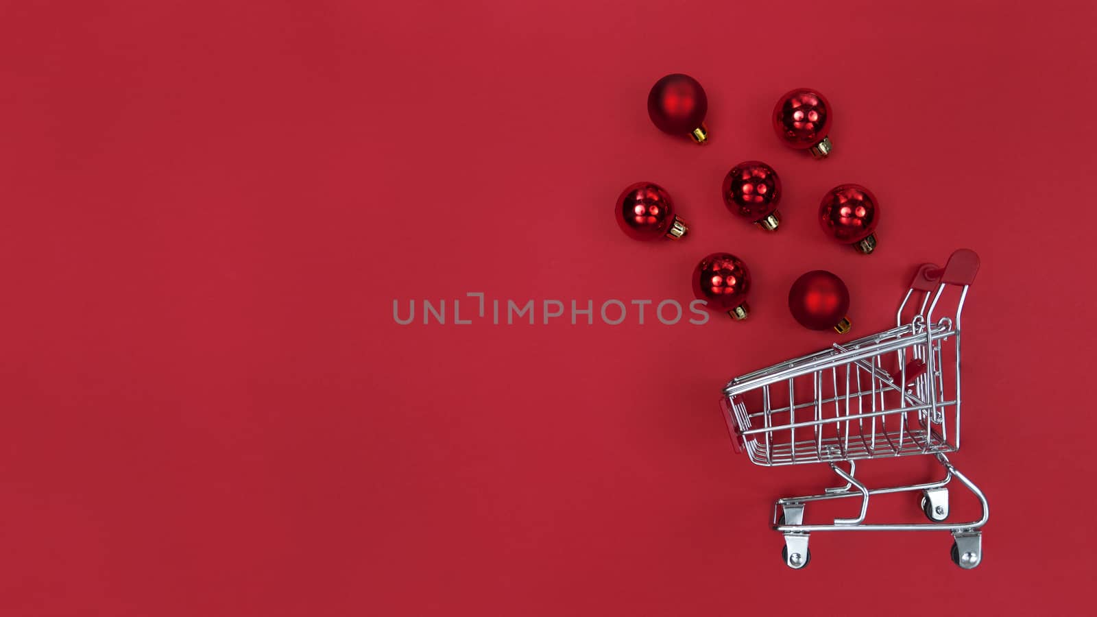 Supermarket trolley and Christmas tree baubles on red paper.