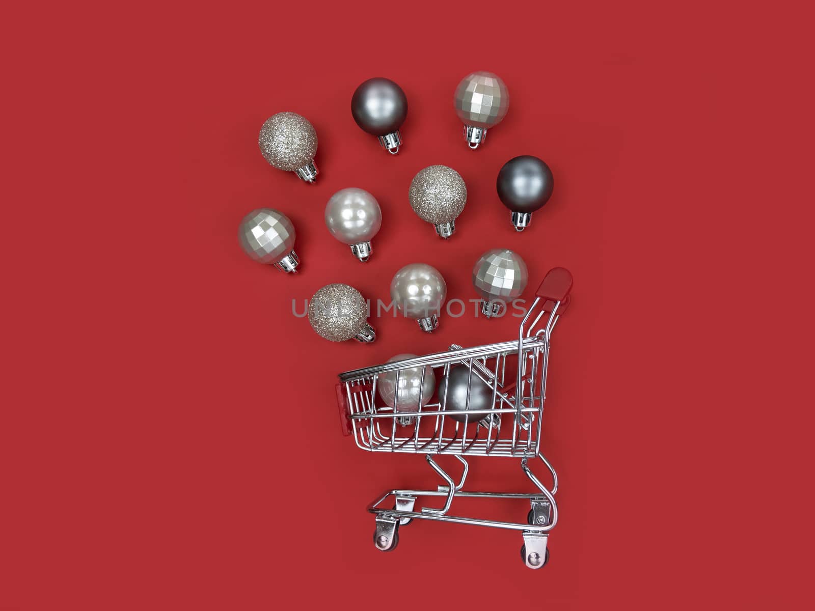 Supermarket trolley and Christmas tree baubles on red paper.