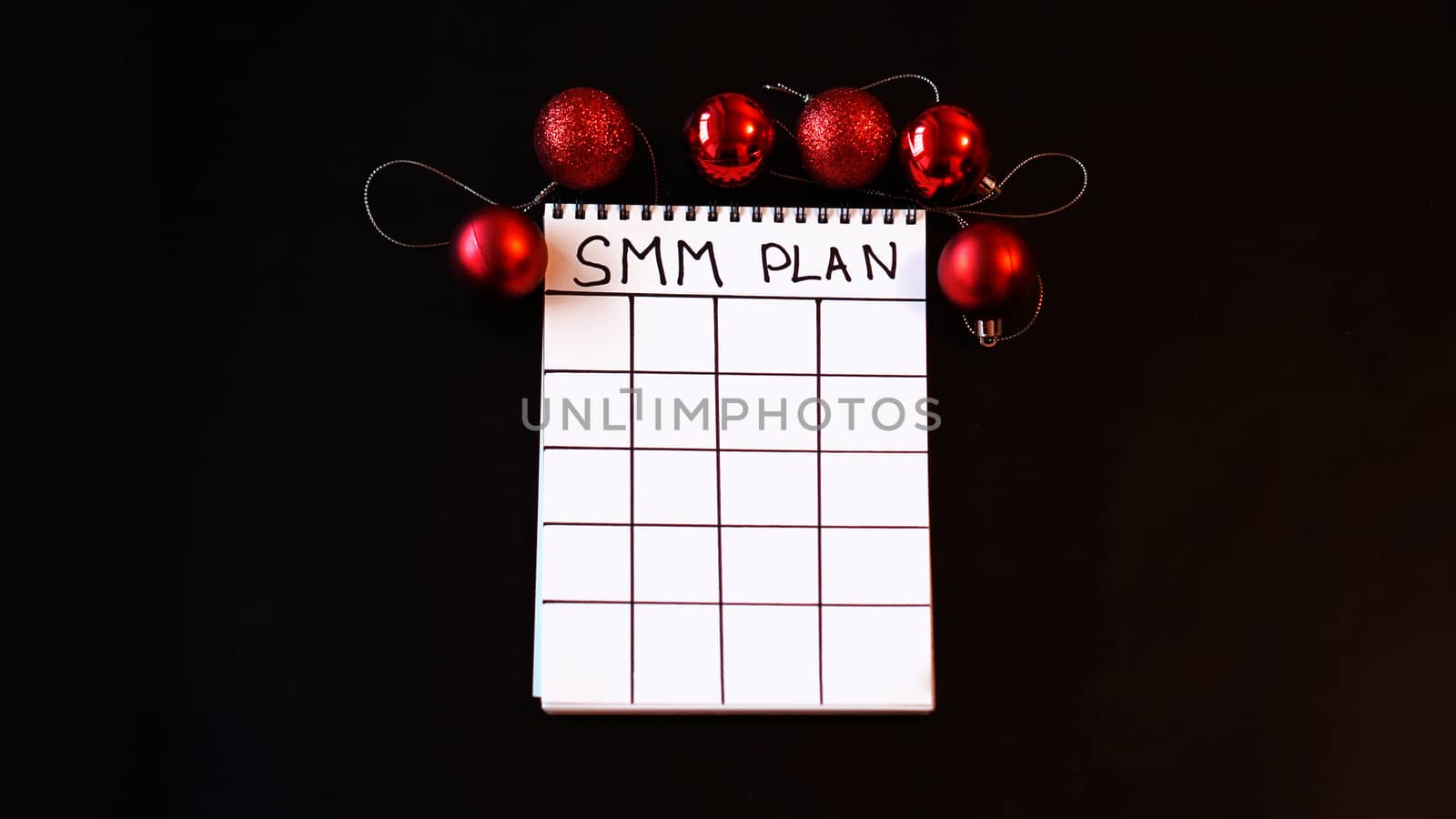 Freelance project. SMM plan blank. White sheet on a black festive background with red Christmas balls