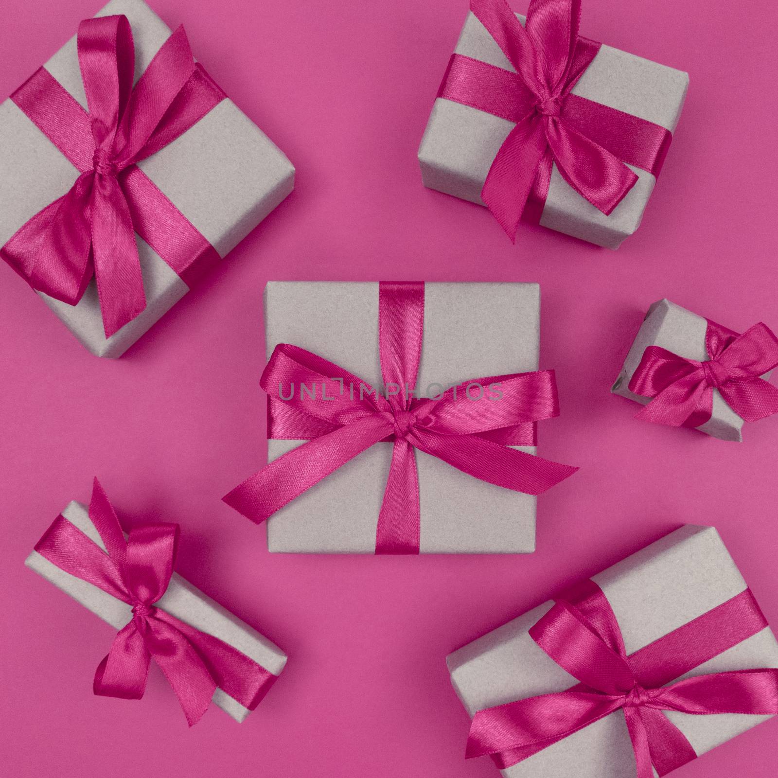 Gift boxes wrapped in a craft paper with pink ribbons and bows. Festive monochrome flat lay.