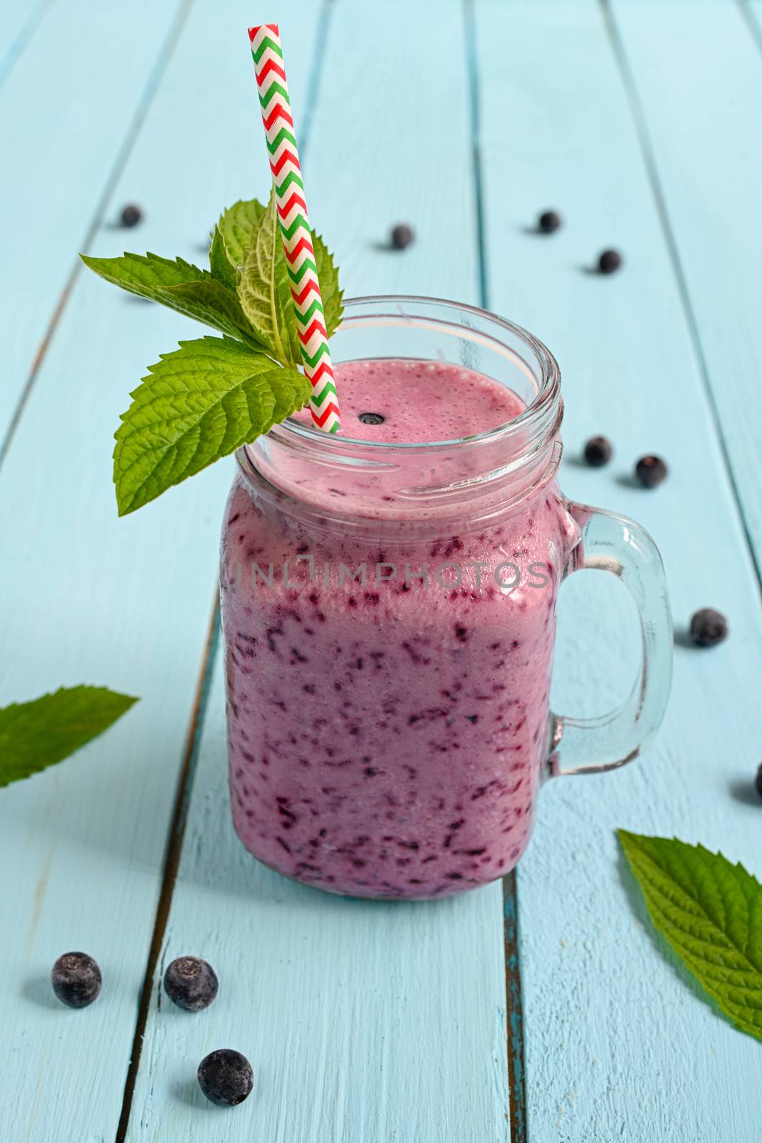 Blueberry smoothie with mint in mason jar with straw against a wood background.