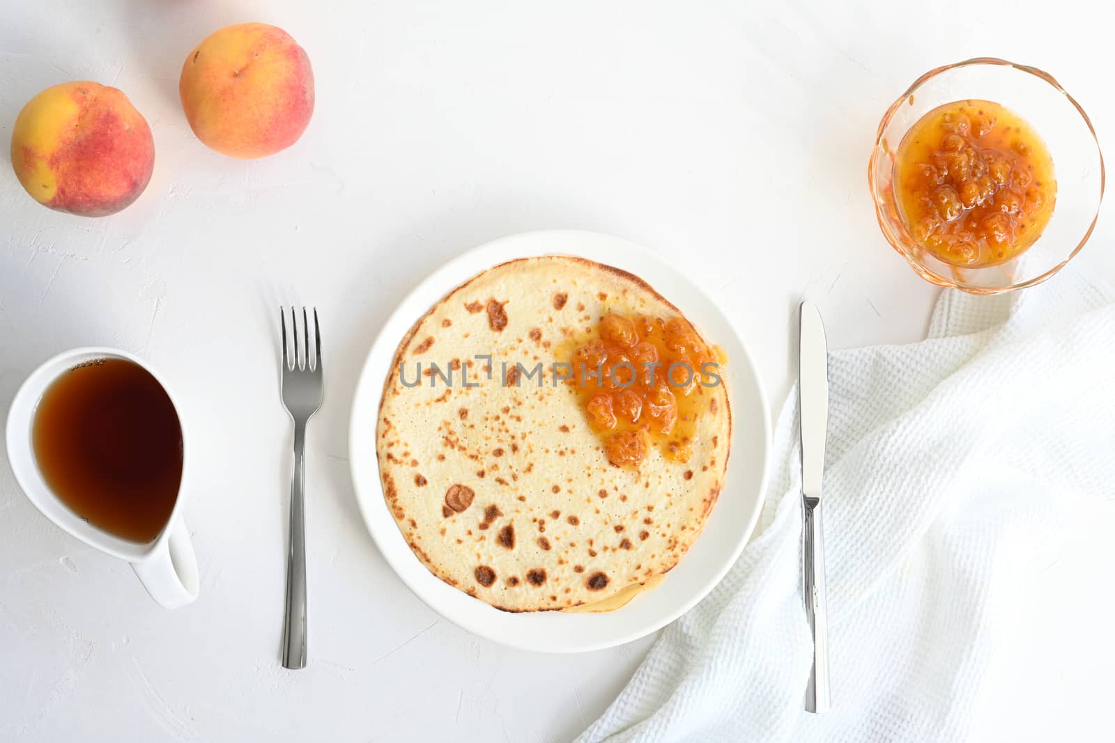 large pancakes with jam, tea and peaches on white background.