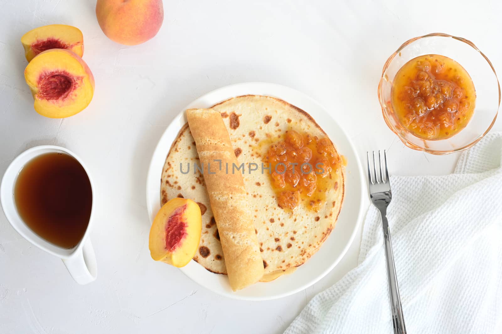 large pancakes with jam, tea and peaches on white background by sashokddt