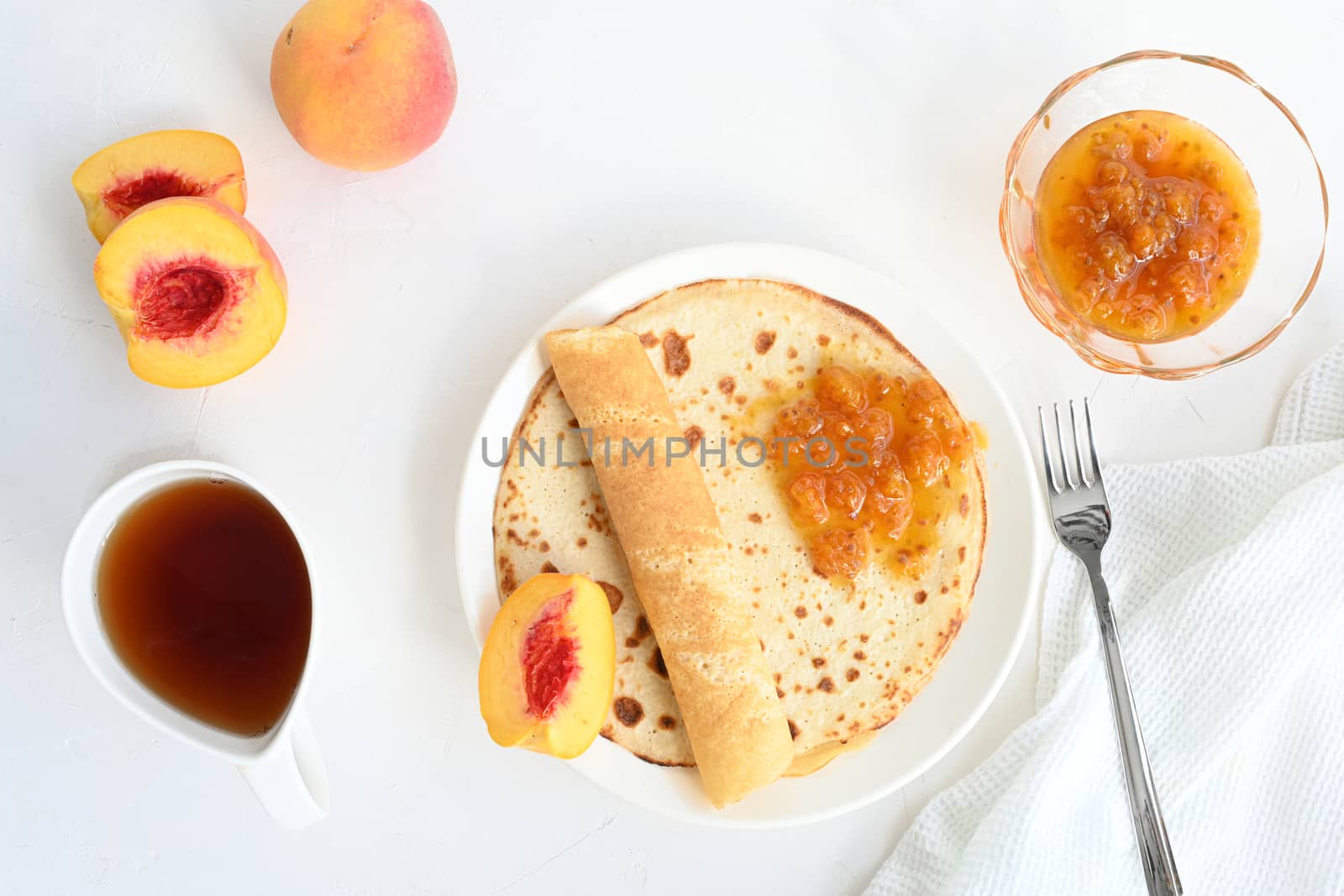 large pancakes with jam, tea and peaches on white background.