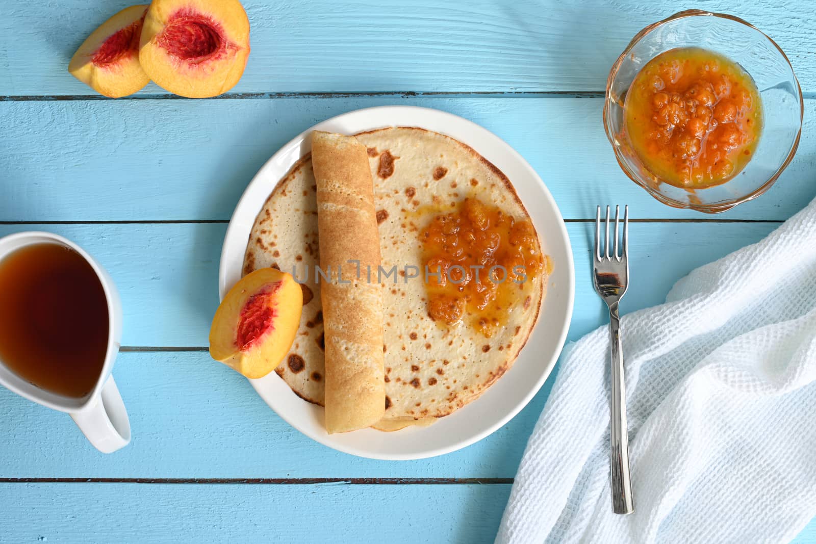 large pancakes with jam, tea and peaches on blue by sashokddt