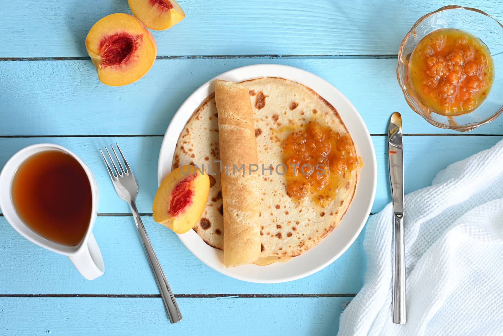 large pancakes with jam, tea and peaches on blue background.