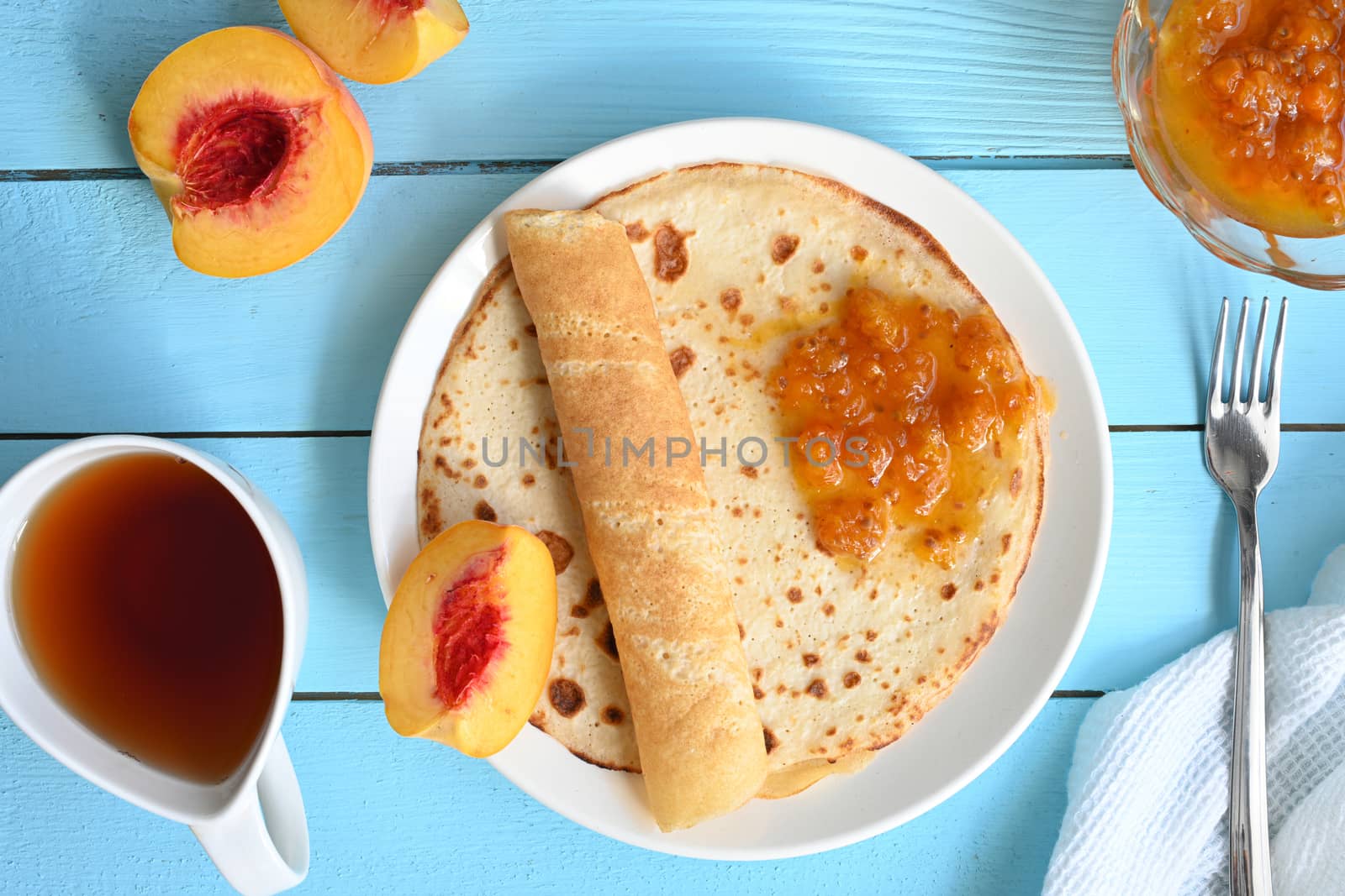 large pancakes with jam, tea and peaches on blue background.