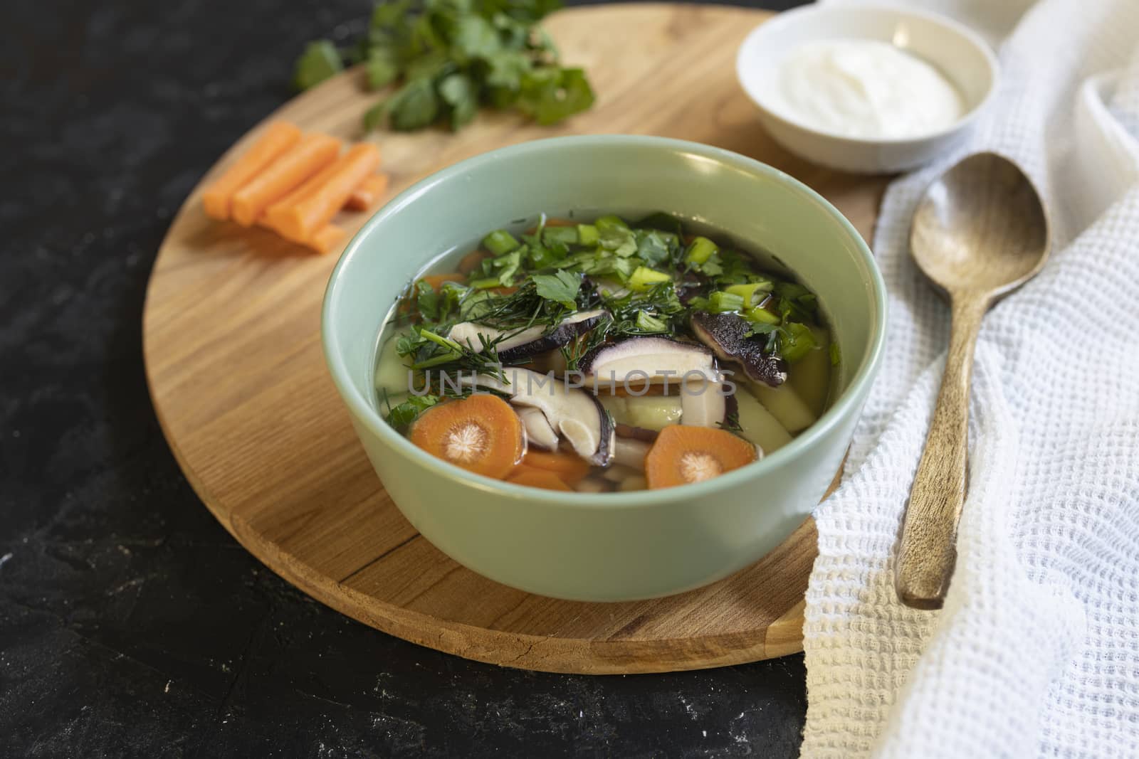 Soup with fresh white mushrooms and potato - traditional dish of russian cuisine in a clay bowl over dark wooden background.Top view with copy space